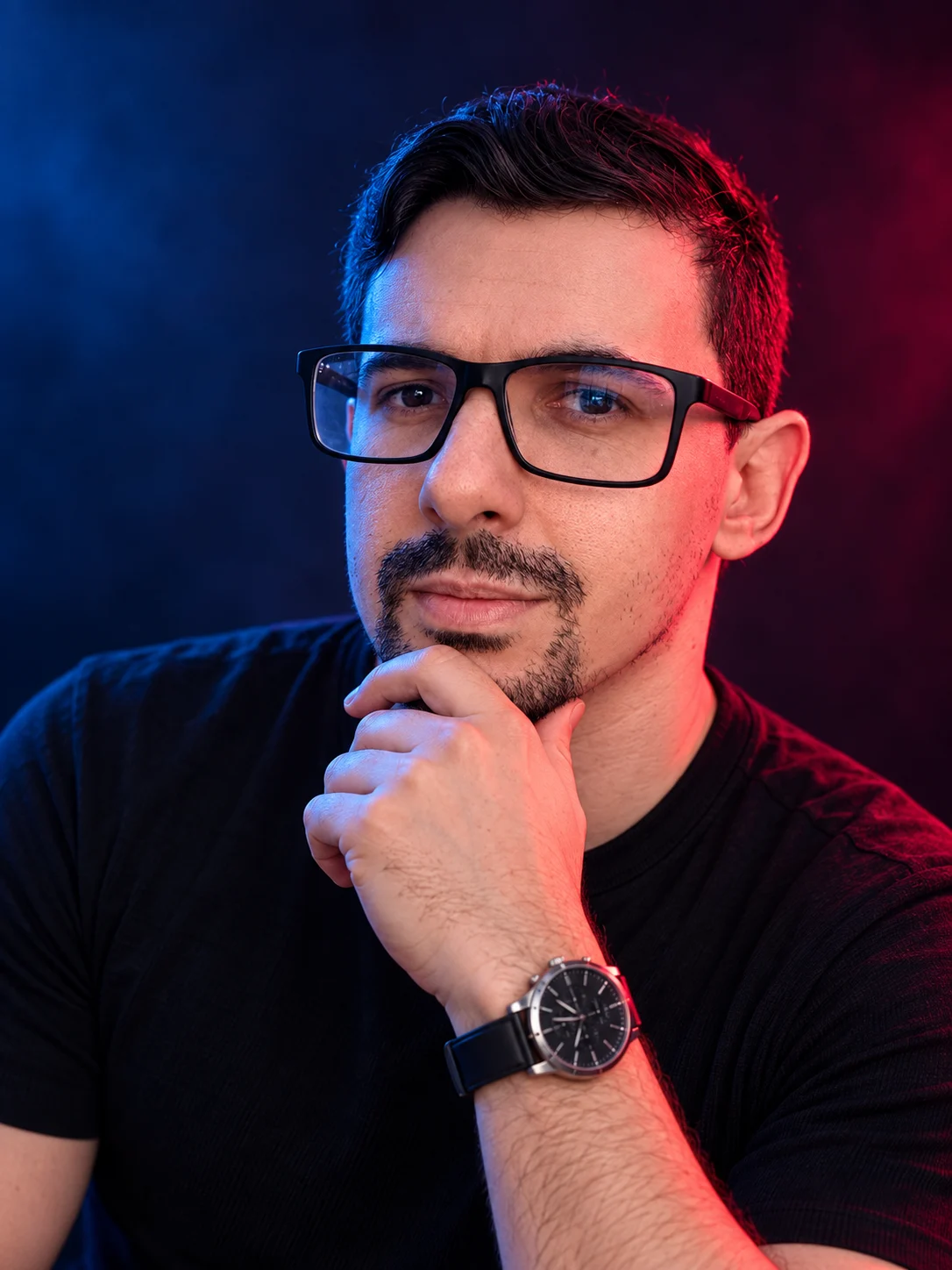 Daniel Paz lit by blue and red neon light, hand on his chin